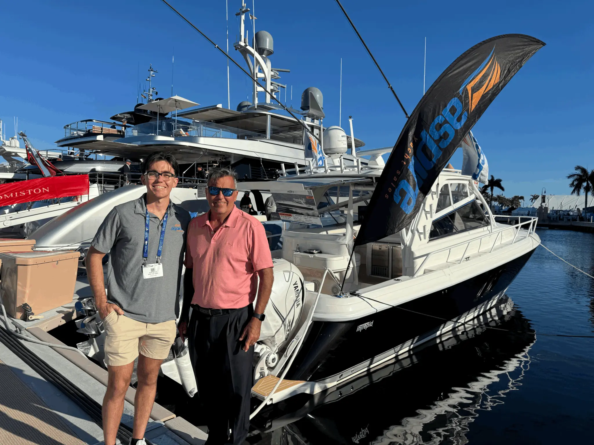 Aspire brokers on the dock at a boat show beside an Intrepid 475 Sport Yacht, the Aspire flag flying